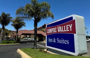 A sign proudly reads Lompoc Valley Inn against a backdrop of swaying palm trees and the inviting hotel facade.