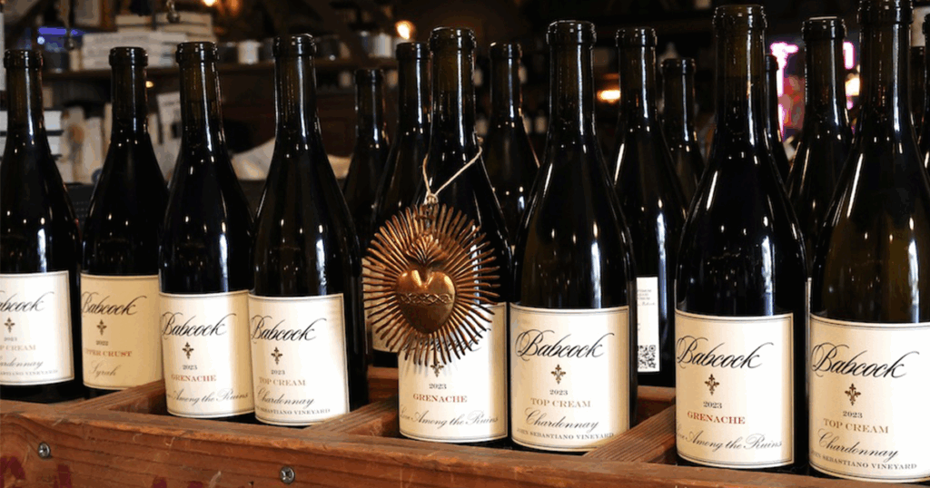 Several bottles of Babcock Vineyards wine are displayed in a row, with a decorative metallic heart ornament hanging on one of the bottles.