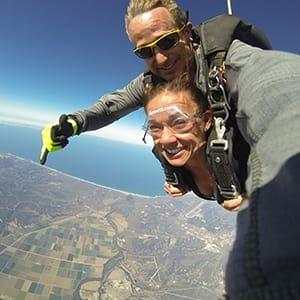 A new skydiver takes a selfie while falling from the sky in tandem and with her certified instructor