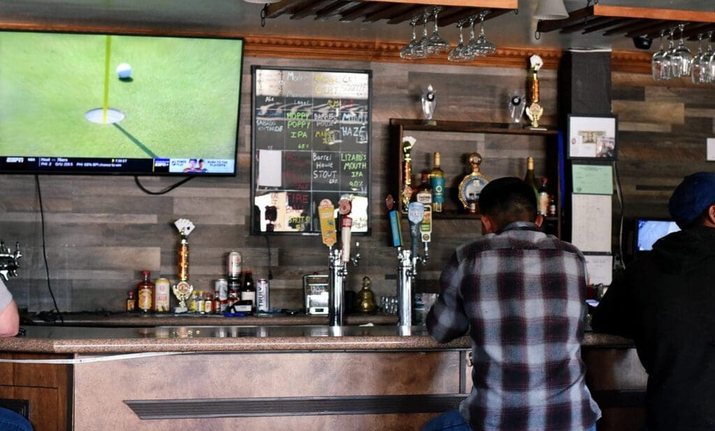 Patrons sit at the bar watching golf at the Tap and Cork Bar