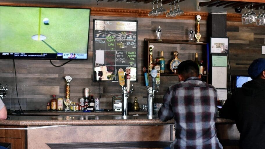 Patrons sit at the bar watching golf at the Tap and Cork Bar