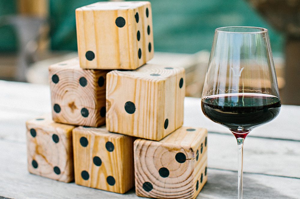 Giant wooden dice stacked in a pyramid sit next to a tall wine glass, half-full of red wine