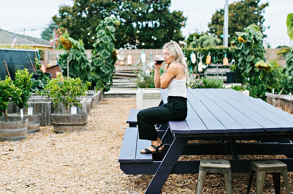 A woman seated on an oversized picnic table enjoys her wine at Montemar Winery