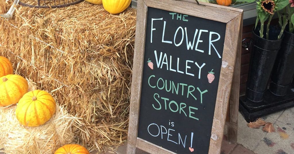 A fall tableau with gourds and hay bales; sign reads: 'Flower Valley Country Store Open!'