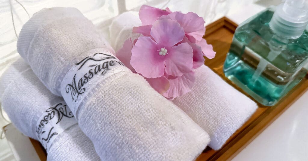 Rolled white towels and a pink flower rest elegantly on a wooden tray beside a pump bottle of liquid soap, creating the perfect spa ambiance.