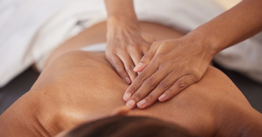 Person receiving a soothing massage from expert hands, lying face down on a massage table draped with a white towel. The experience promises to revitalize the spokenbody and renew ones sense of well-being.