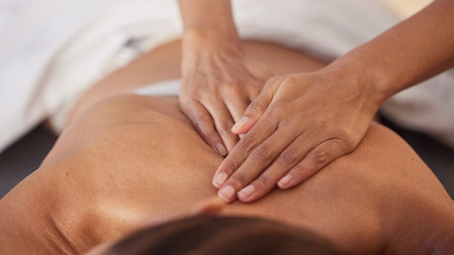 Person receiving a soothing massage from expert hands, lying face down on a massage table draped with a white towel. The experience promises to revitalize the spokenbody and renew ones sense of well-being.