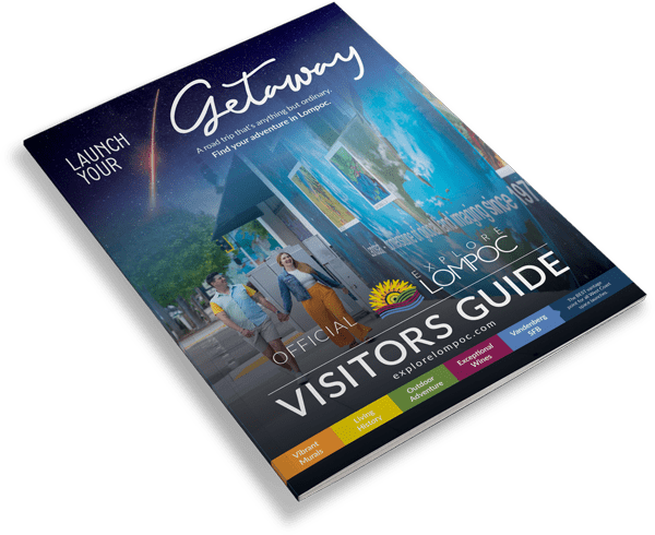 A visitors guide for Lompoc is displayed on a surface. The cover features colorful graphics and the text Launch Your Getaway alongside a website address explorelompoc.com.