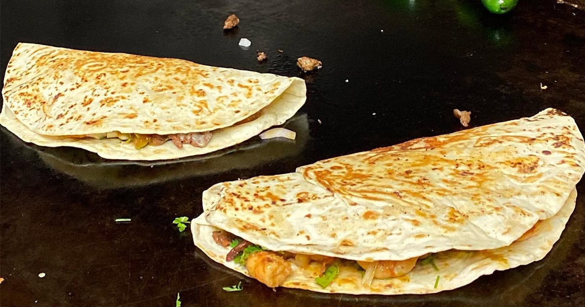 Two folded quesadillas with visible meat and vegetables cooking on a flat grill.