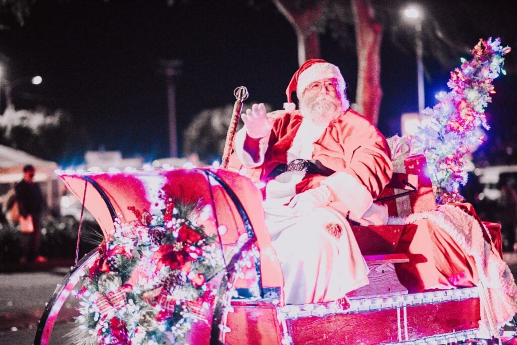 A person dressed as Santa Claus waves from a decorated, festive sleigh at night during Lompoc’s holiday parade, adding to the festive fun of the season.