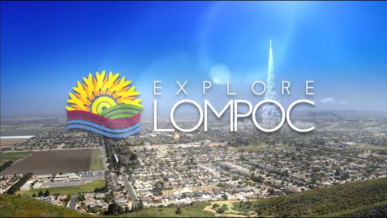Aerial view of Lompoc CA with the words Explore Lompoc and a colorful sun and hills graphic overlaid on the image.