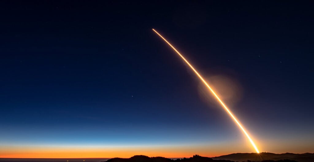 Nighttime rocket launch with bright streak across Lompoc, California sky.