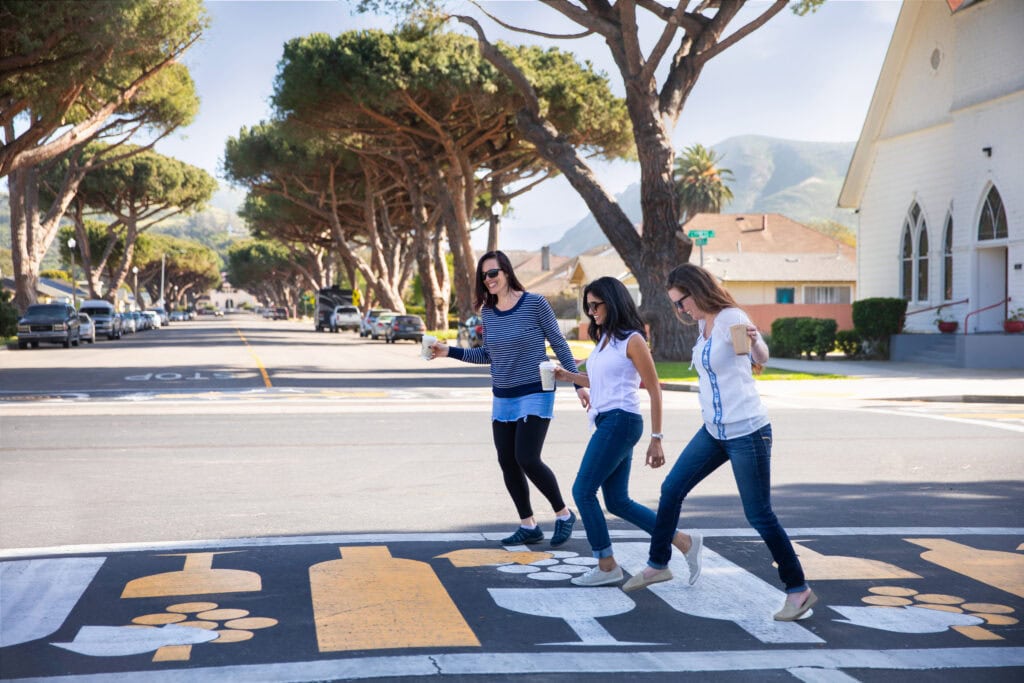 People crossing the street in Lompoc, California with trees and buildings in the background.