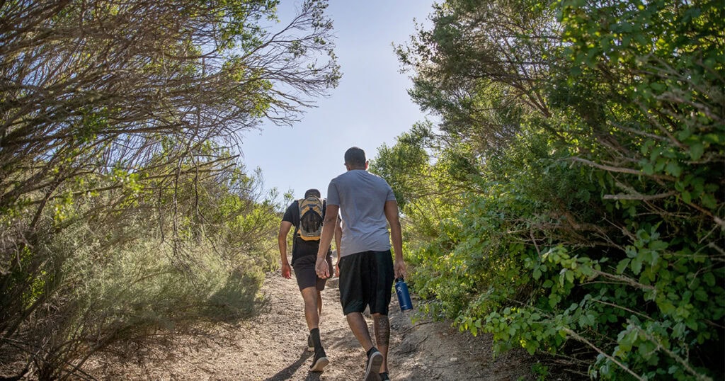 Two hikers walking on a trail surrounded by lush greenery in Lompoc, California.