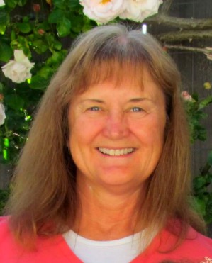 Smiling woman with brown hair in front of flowering bushes in Lompoc.